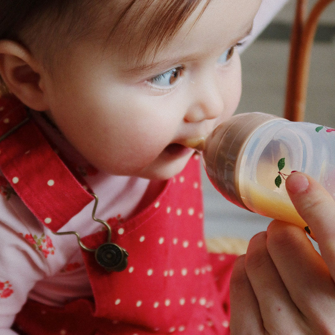 Een baby wordt gevoed met de Konges Sløjd voedingsfles met lepelopzetstuk.