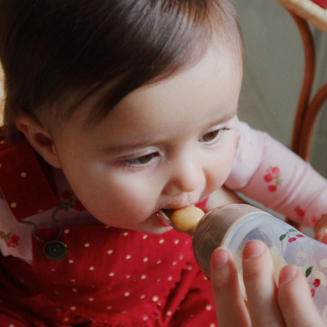 Close-up van een baby die gevoed wordt met de Konges Sløjd voedingsfles met lepel.