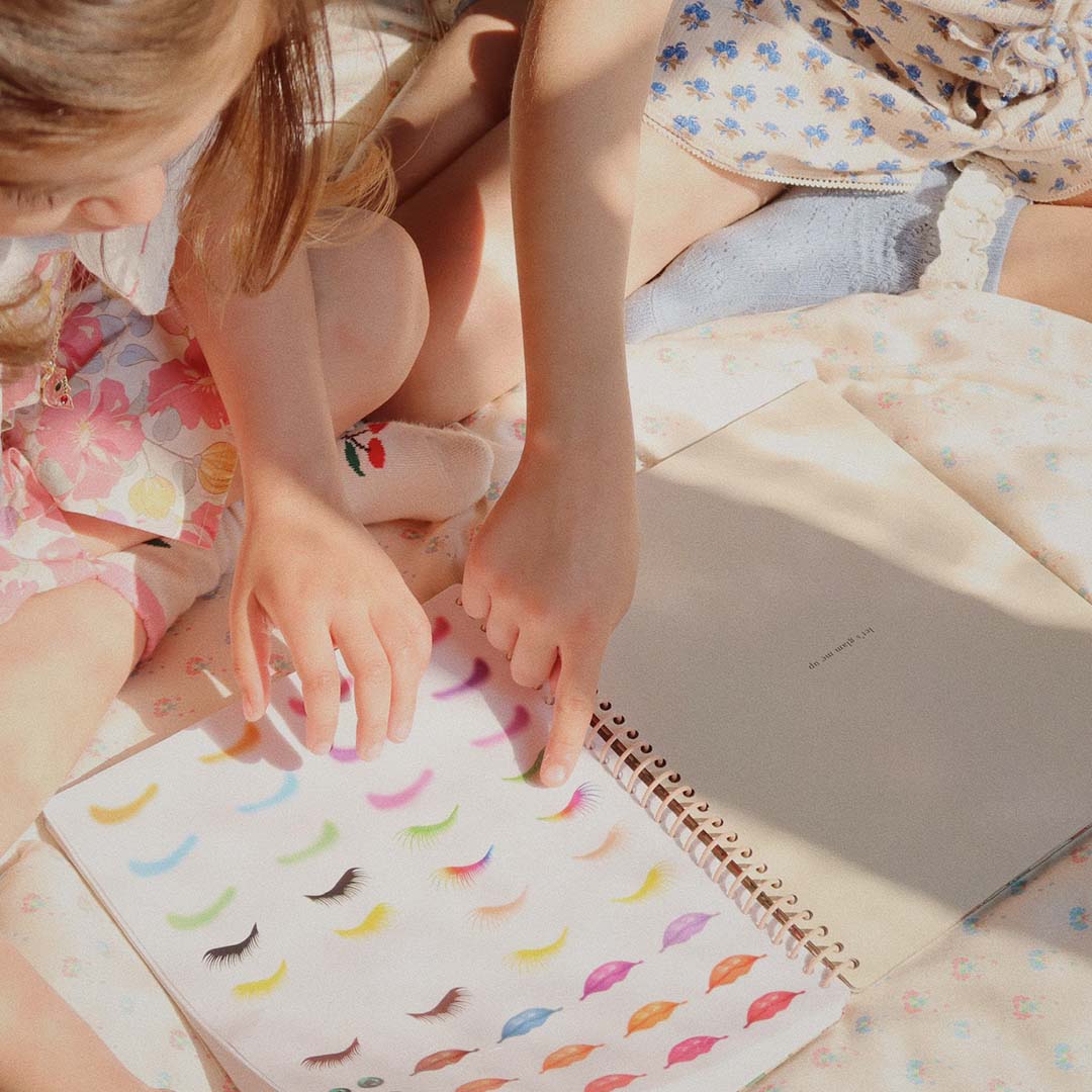 Twee kinderhanden die wijzen naar een pagina in het stickerboek met kleurrijke wimperstickers.