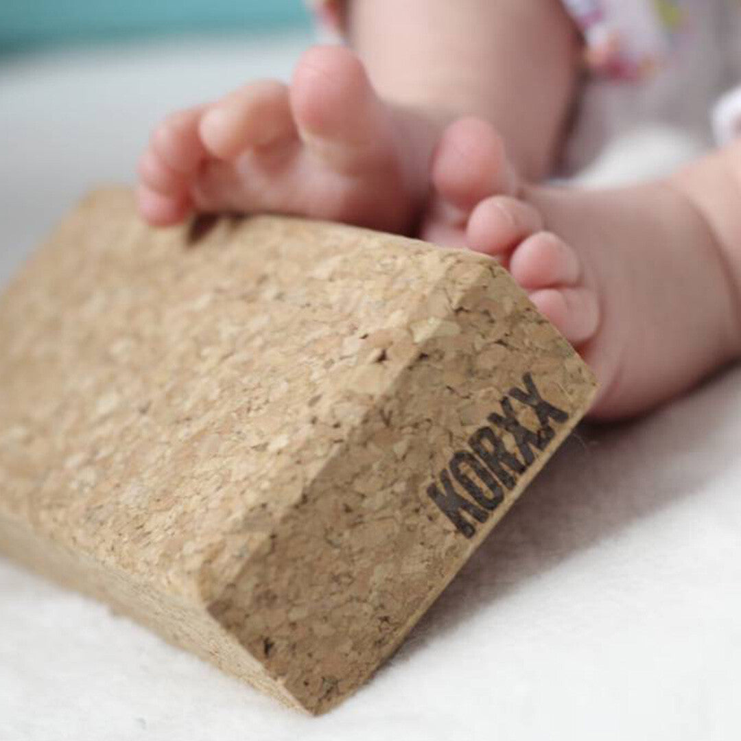 Een KORXX kurk baby bouwblok op de voorgrond met de voetjes van een baby op de achtergrond.