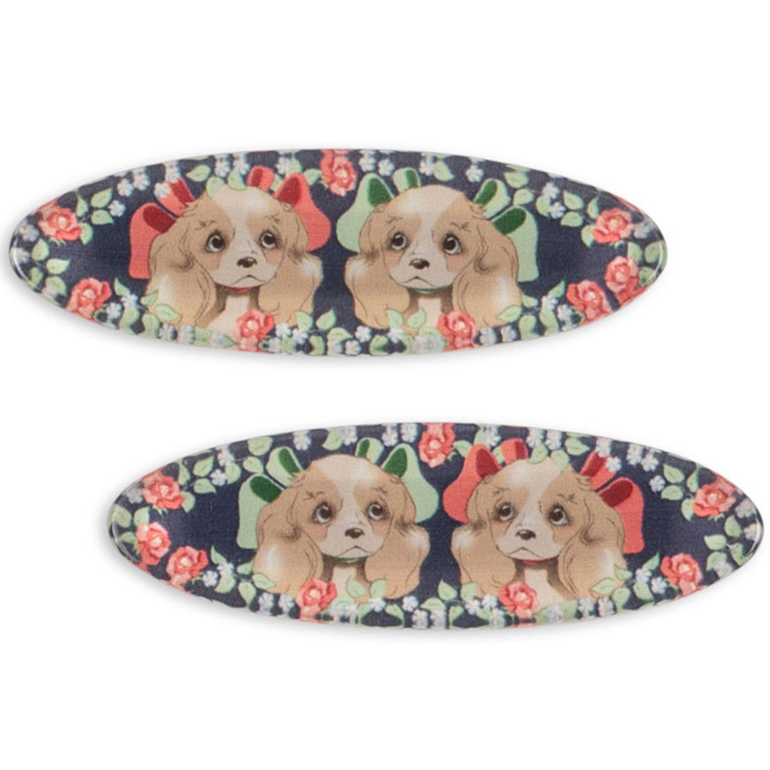Twee Konges Sløjd haarclips met een patroon van puppy's met strikken en rozen op een donkerblauwe achtergrond.