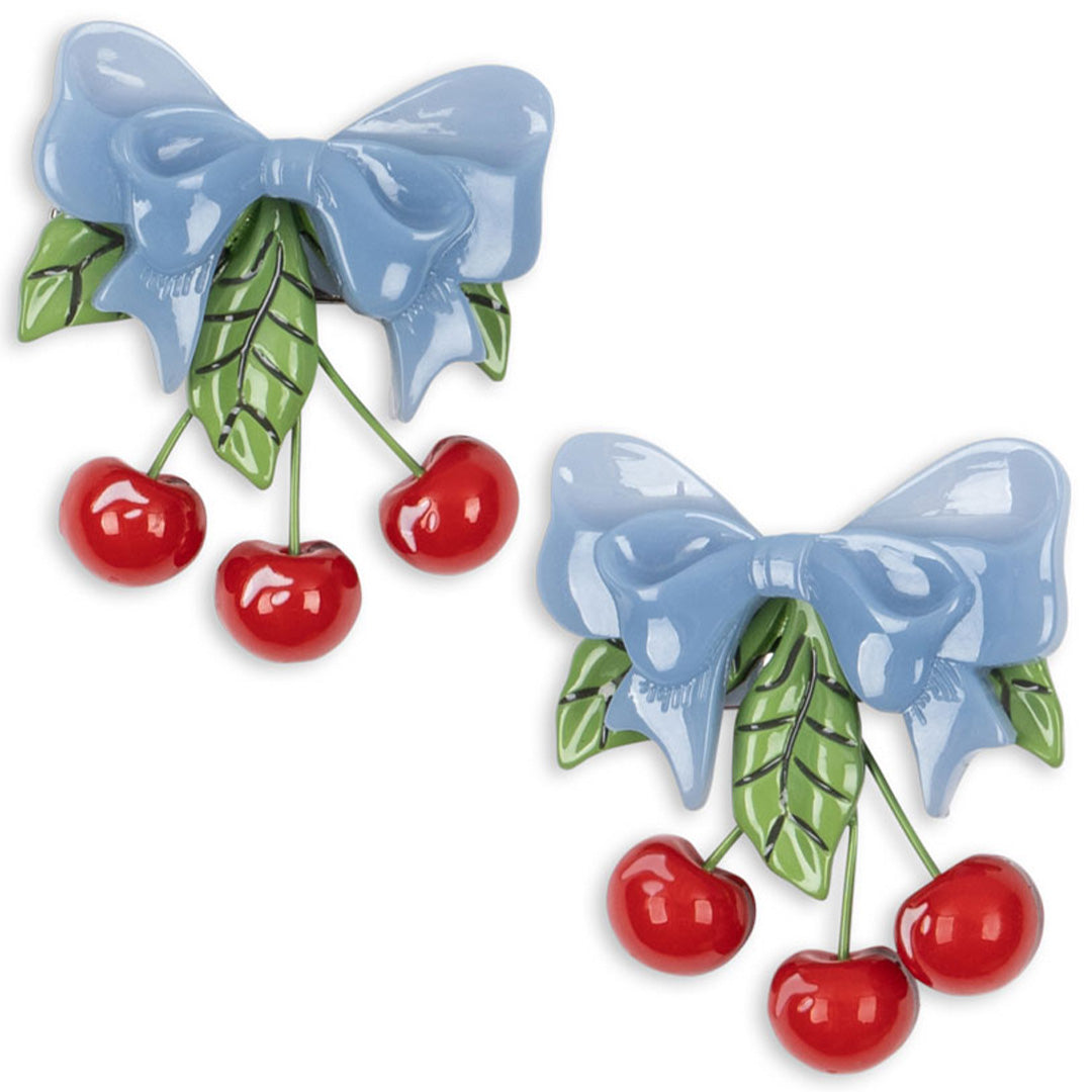 Twee Konges Sløjd kinder haarclips met een blauwe strik, groene bladeren en rode kersen.