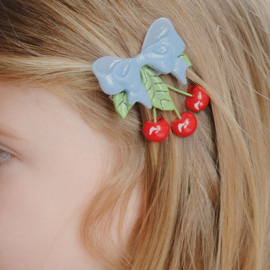 Een Konges Sløjd kinder haarclip met blauwe strik en rode kersen in het blonde haar van een kind.