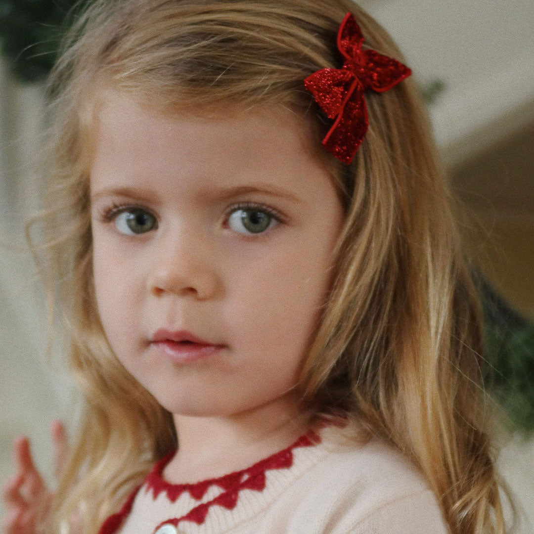 Een kind met blond haar draagt een rode glitter haarclip aan de zijkant van haar hoofd.