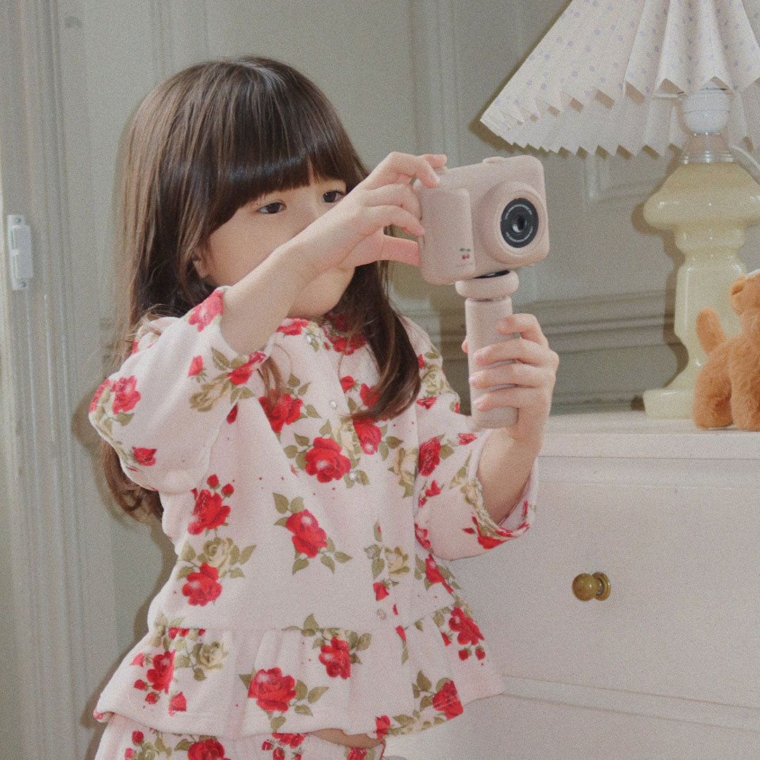 Een meisje in een roze bloemenoutfit houdt de kindercamera vast en kijkt ernaar.
