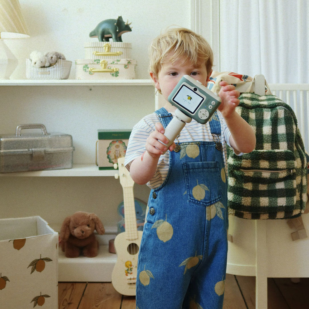 Een kind in een spijkerbroek met citroenen houdt de Konges Sløjd kindercamera vast in een kinderkamer.