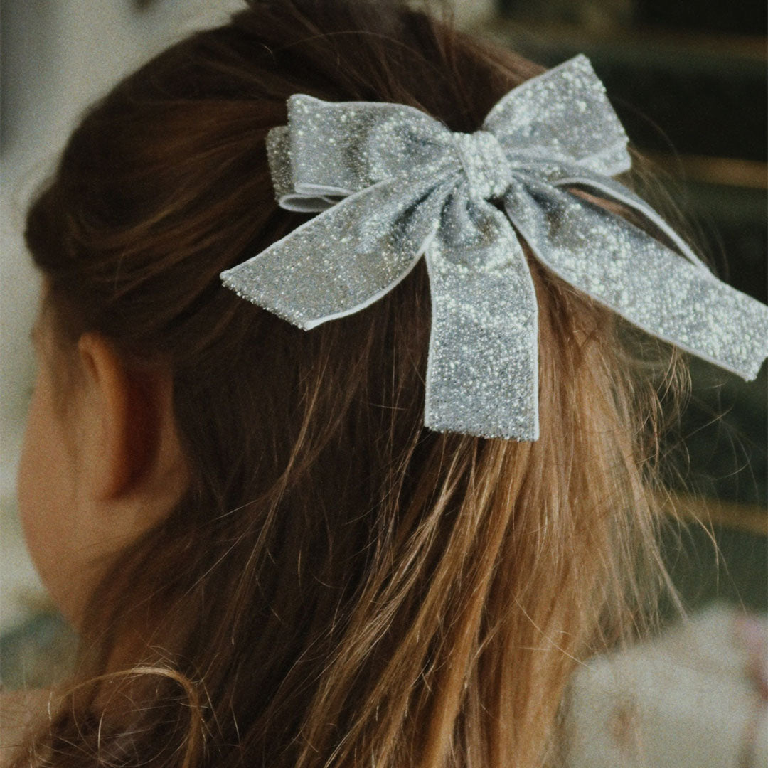 Zilveren glitter fluwelen haarclip in het haar van een kind, van achteren gezien.