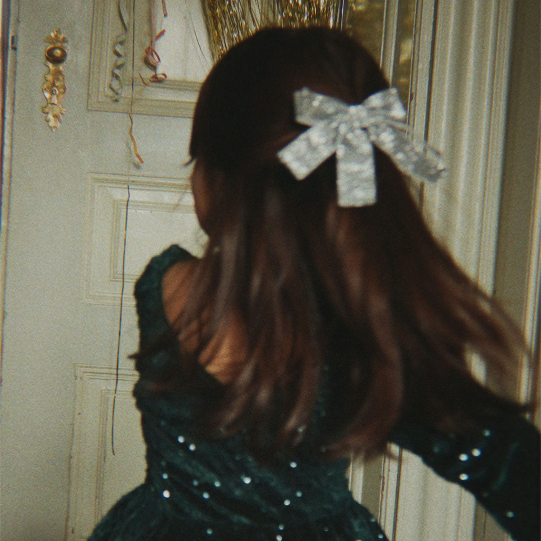 Kind met zilveren glitter fluwelen haarclip in het haar, kijkend naar een versierde deur.