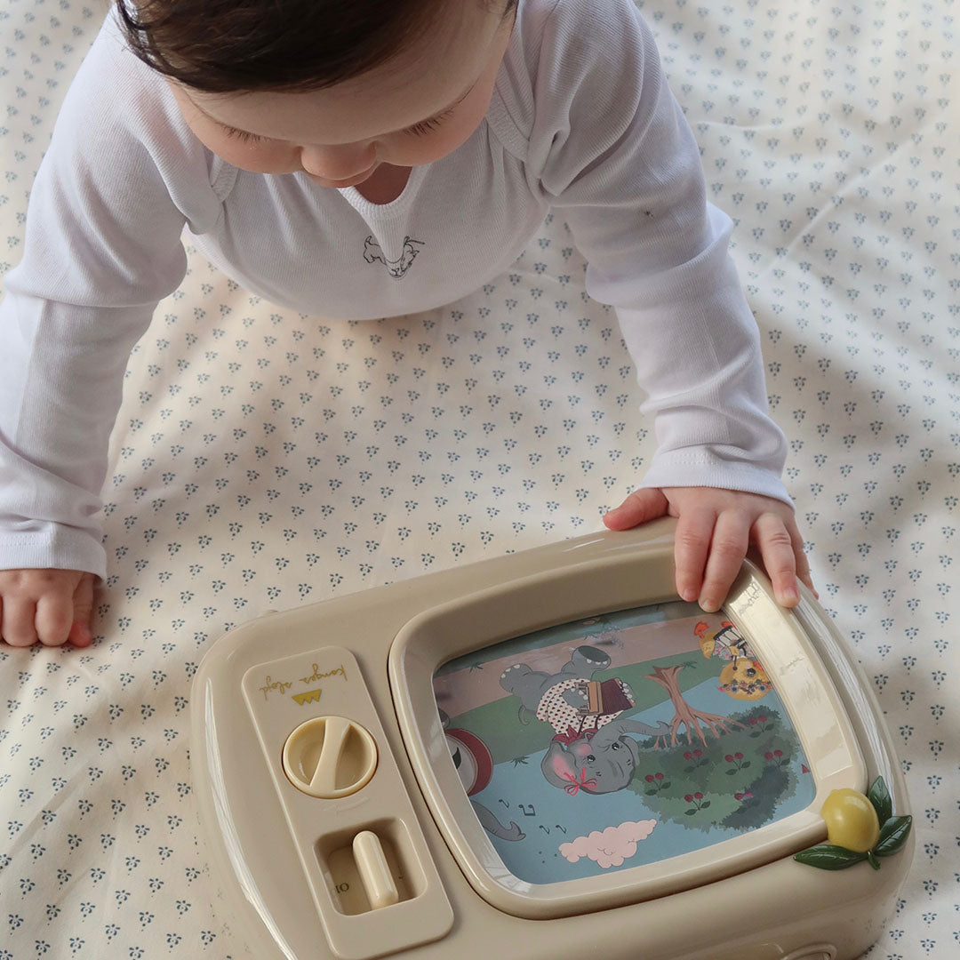 Een baby reikt naar de beige muziek tv speeldoos met een scherm waarop dieren te zien zijn.
