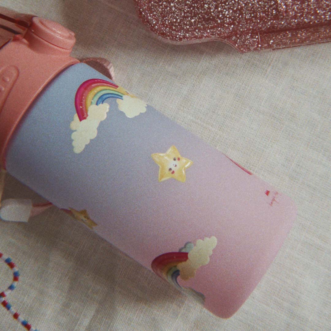 Drinkfles met regenboog- en sterrenpatroon, liggend op een lichte stof.