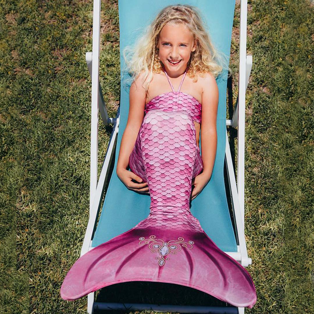 Een meisje ligt op een blauwe ligstoel en draagt een kuaki mermaids roze zeemeerminstaart.
