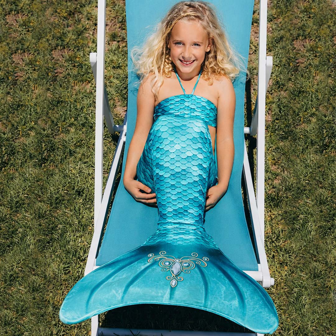 Lachend meisje ligt op een ligstoel en draagt een kuaki mermaids turquoise zeemeerminstaart.