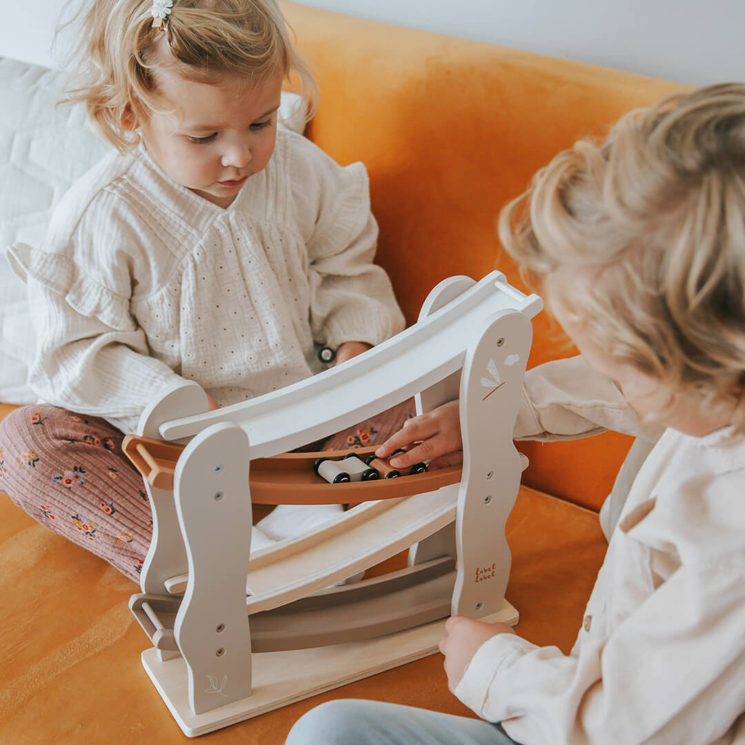 Twee kinderen spelen met de Label Label houten autobaan op een oranje bank.