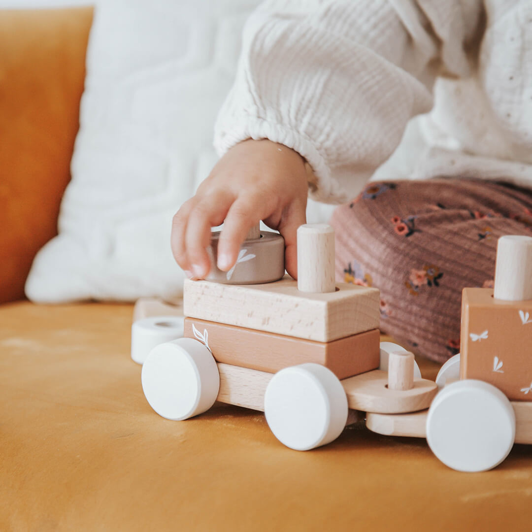Een kinderhand plaatst een blok op een wagon van de Label Label houten blokkentrein.