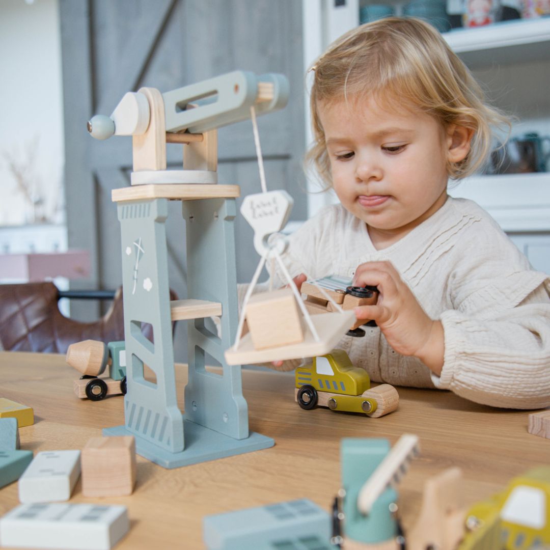 Een jong kind speelt met de Label Label houten bouwset, waarbij ze een blok met de kraan optilt.