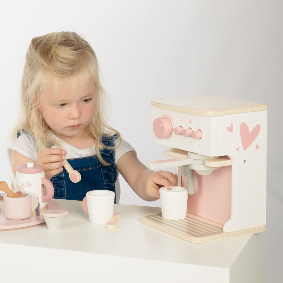 Een jong meisje speelt met het label label houten speelgoed koffiezetapparaat, waarbij ze een kopje onder de dispenser houdt.