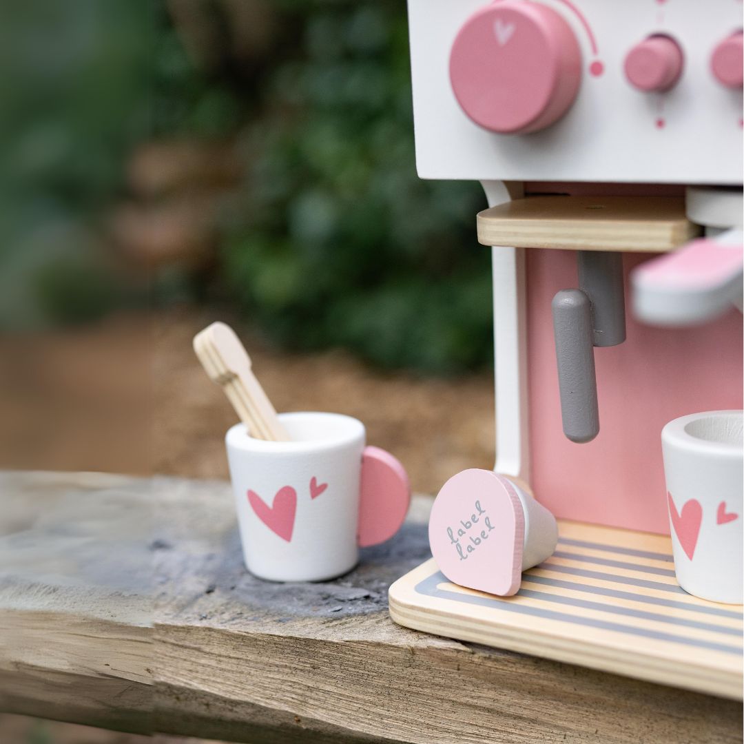 Detail van het label label houten speelgoed koffiezetapparaat met een roze-wit kopje met harten en een koffiepad.