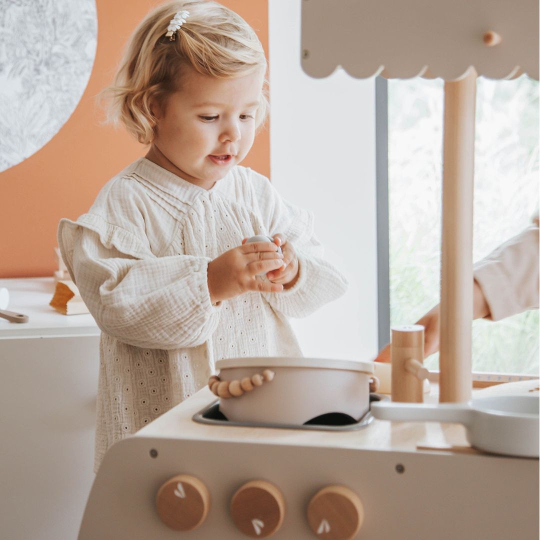 Een kind speelt met een potje op de Label Label houten kinderkeuken bistro.
