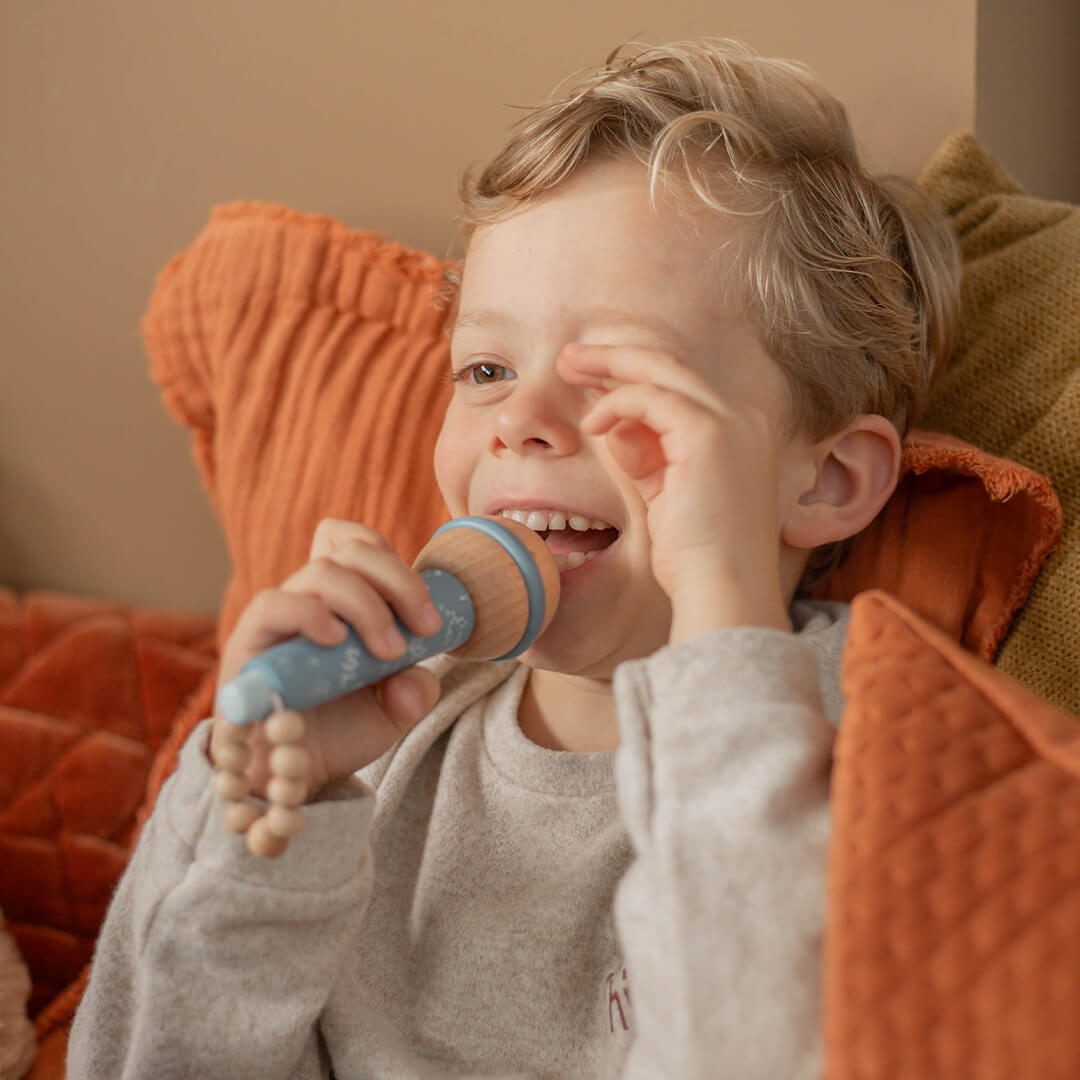 Een lachende jongen zingt in de label label houten speelgoedmicrofoon.