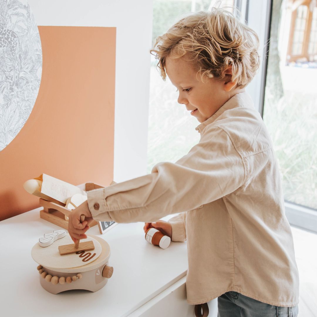 Een jongen speelt met de houten pannenkoekenmaker speelset op een witte tafel.