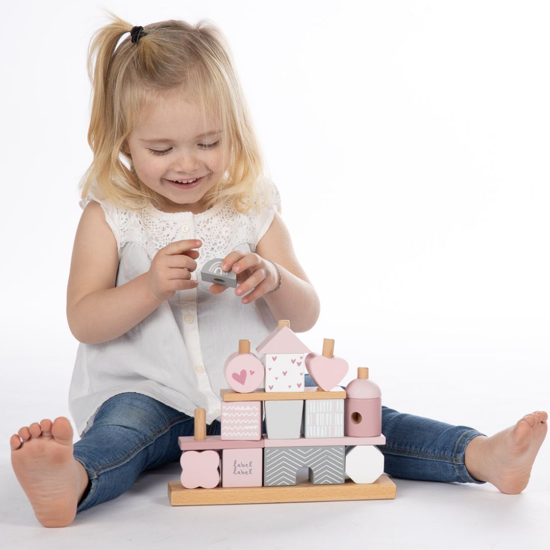 Een lachend meisje speelt op de grond met de label label houten bouwblokken set.