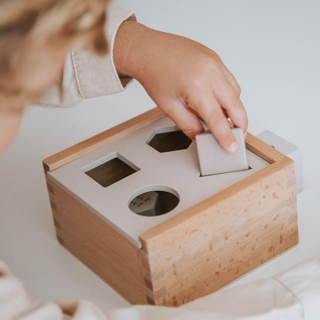 Een kinderhand plaatst een blokje in de label label houten vormenstoof.