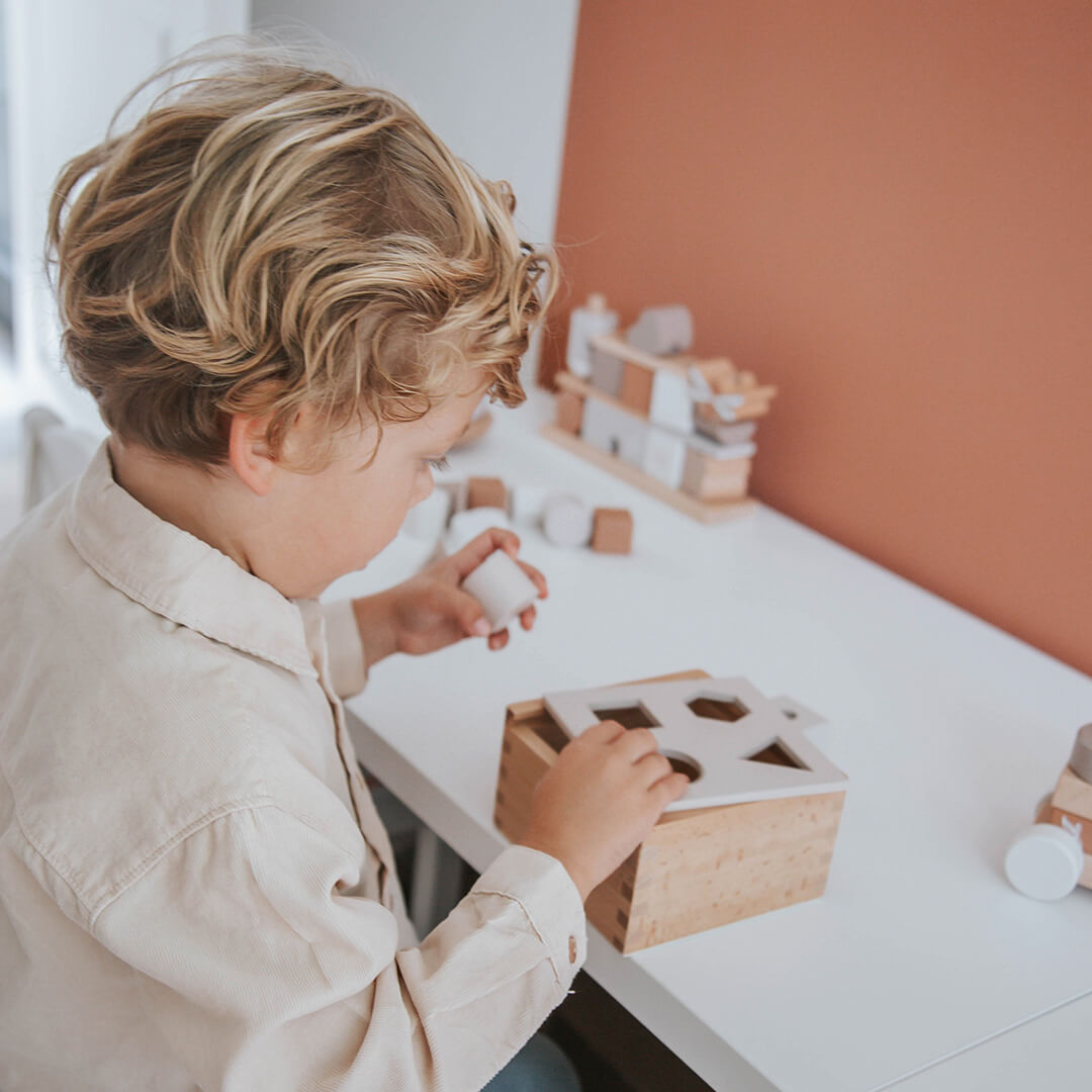 Een kind speelt met de label label houten vormenstoof aan een witte tafel.
