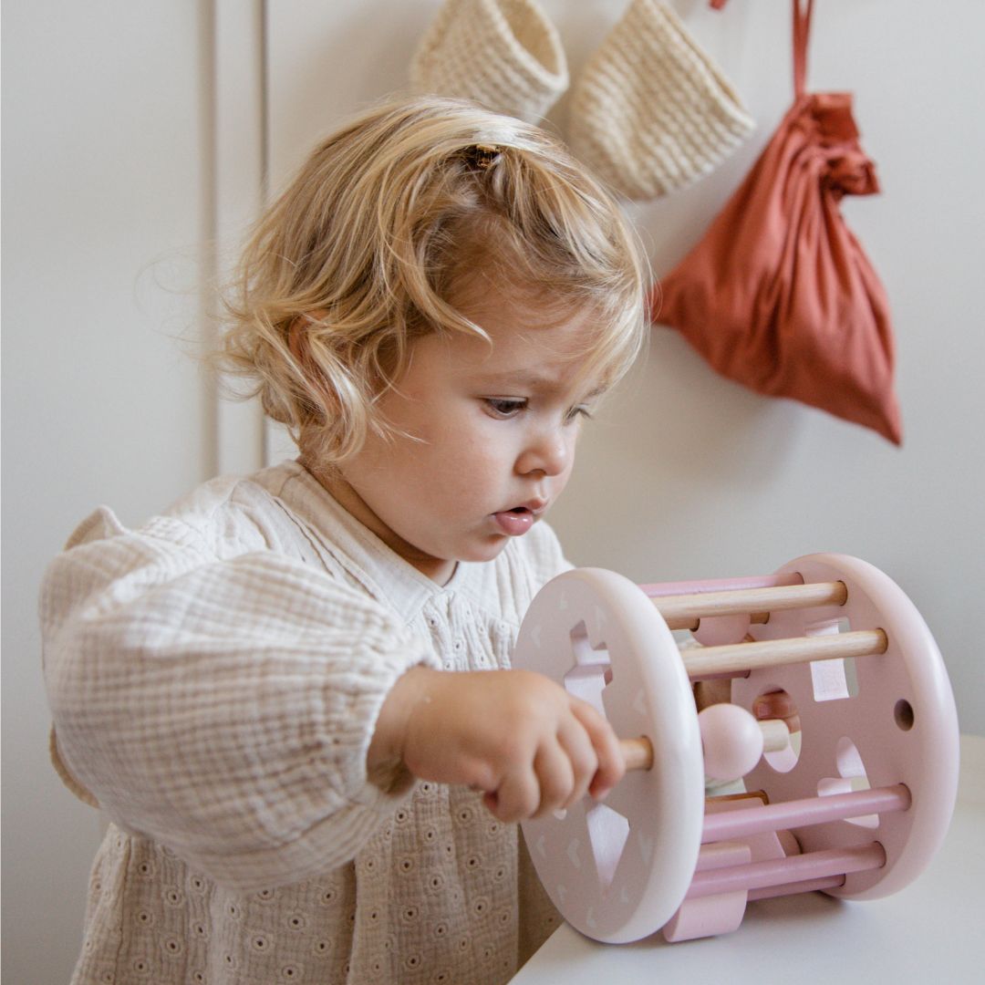 Een peuter speelt met het label label roze houten vormsorteerwiel.