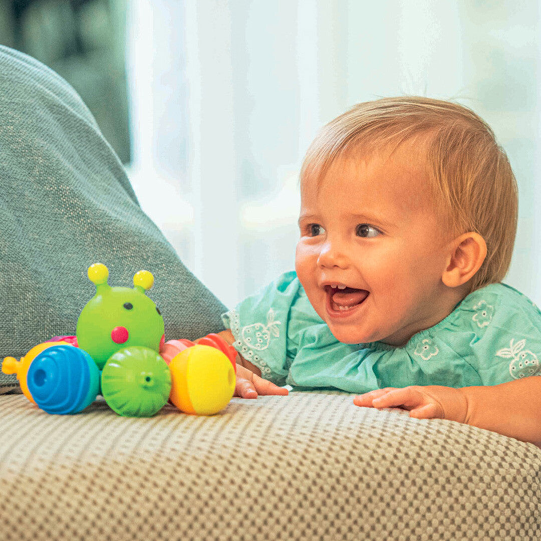 Een lachende baby speelt met de Lalaboom rups van klikkralen op een bank.