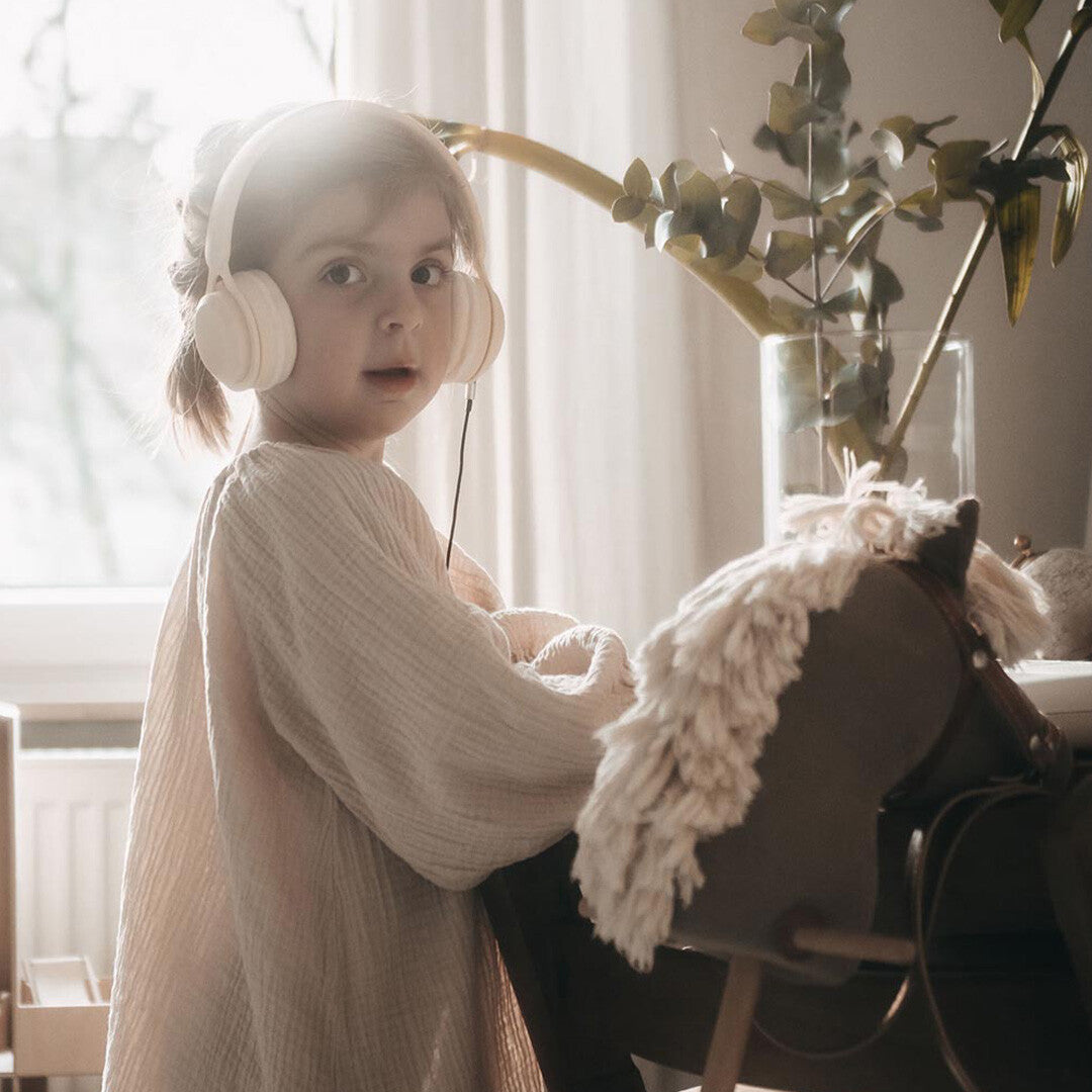 Een kind draagt een lichte kinderkoptelefoon en kijkt in de camera, naast een hobbelpaard.