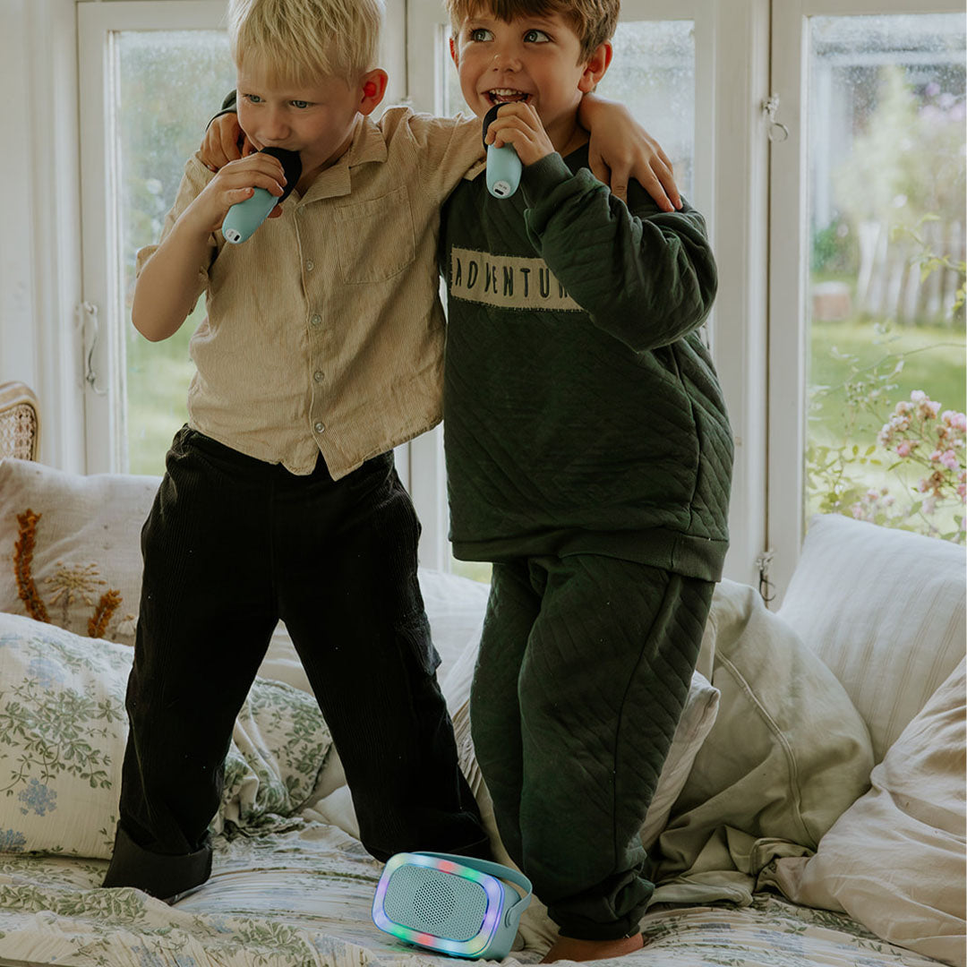 Twee jongens zingen met lalarma copenhagen microfoons bij de lichtgevende karaokespeaker op een bed.