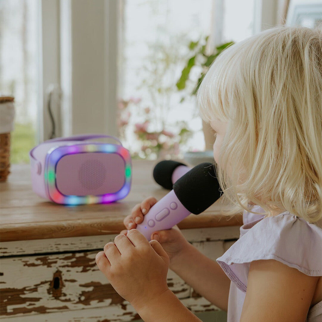 Een kind zingt in een paarse microfoon van de lalarma copenhagen karaokeset, met de lichtgevende speaker op de achtergrond.