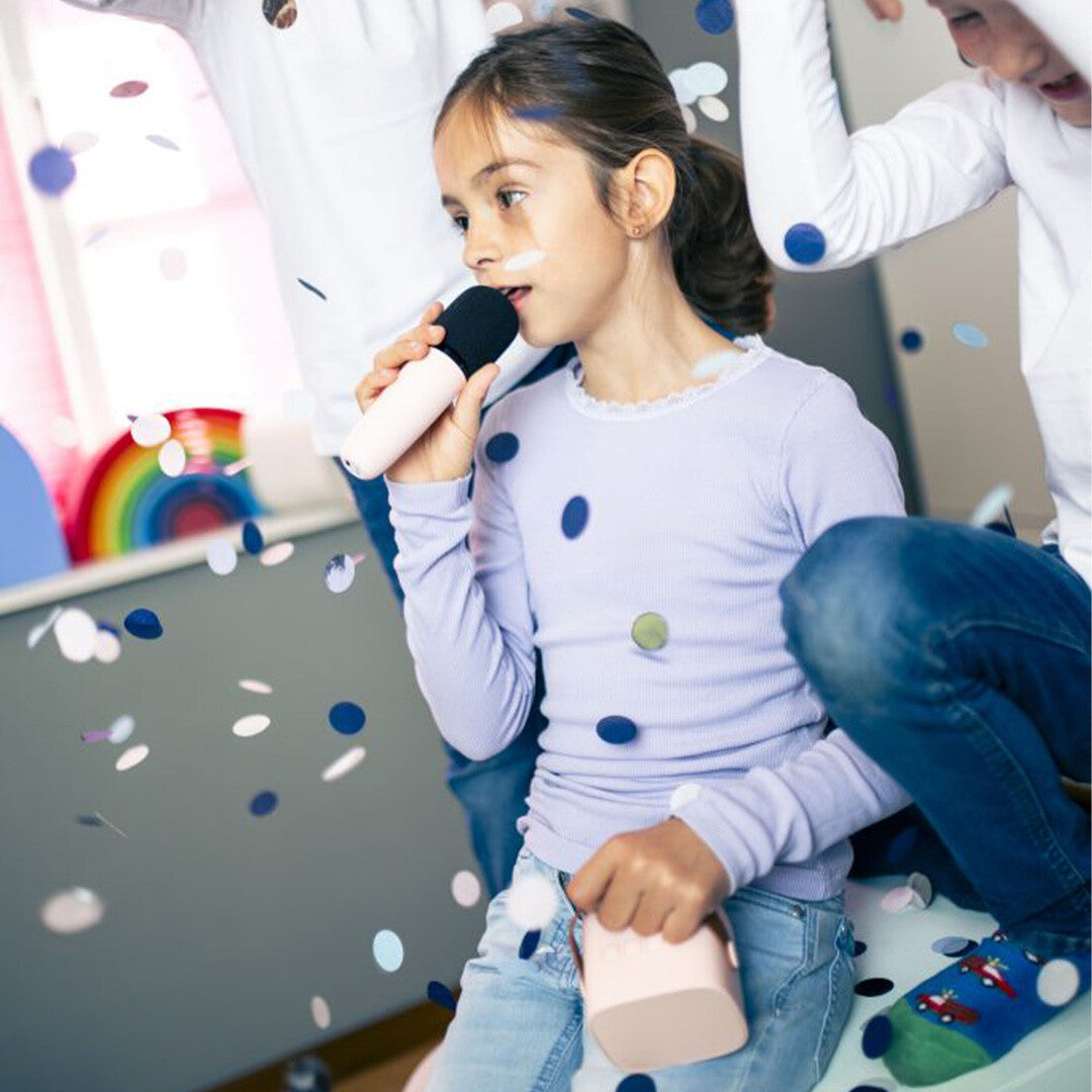 Een meisje zingt in een roze karaokemicrofoon terwijl confetti valt.