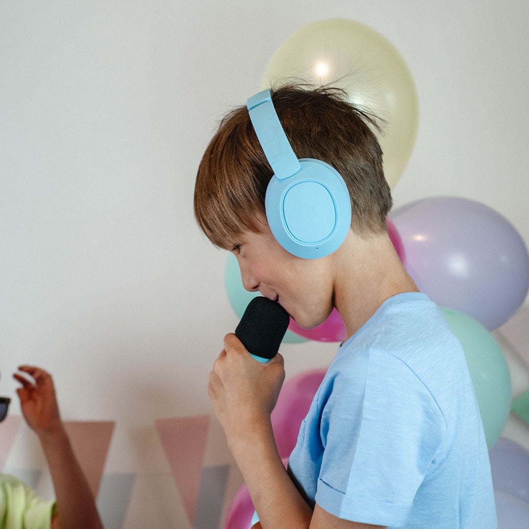 Een jongen met een lichtblauwe lalarma kinderkoptelefoon zingt in een microfoon.