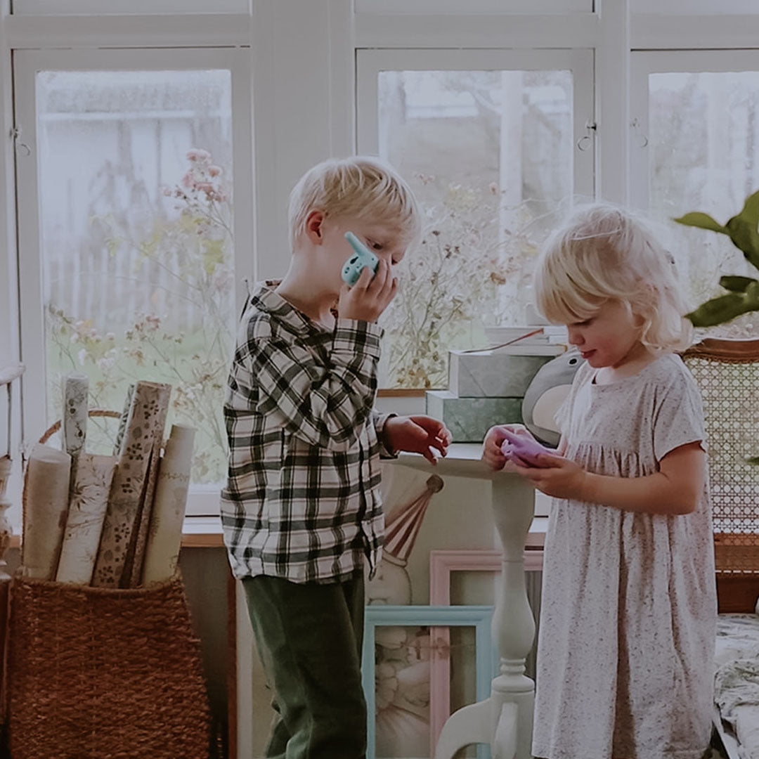 Twee kinderen spelen met lalarma copenhagen walkie talkies, de jongen met een blauwe en het meisje met een roze.