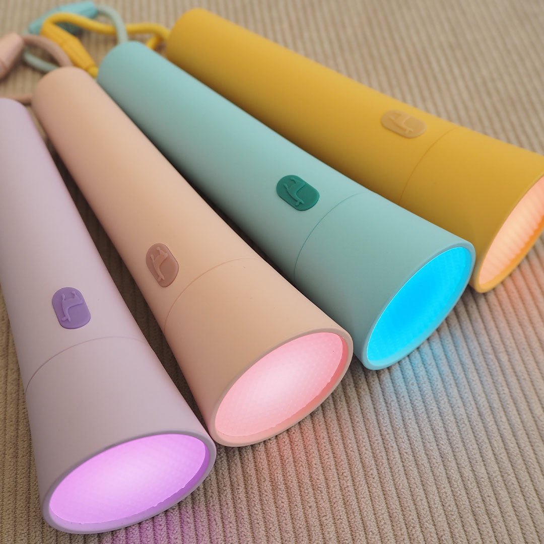 Vier Lalarma zaklampen in pastelkleuren met brandende lampen liggen schuin op een geribbelde ondergrond.