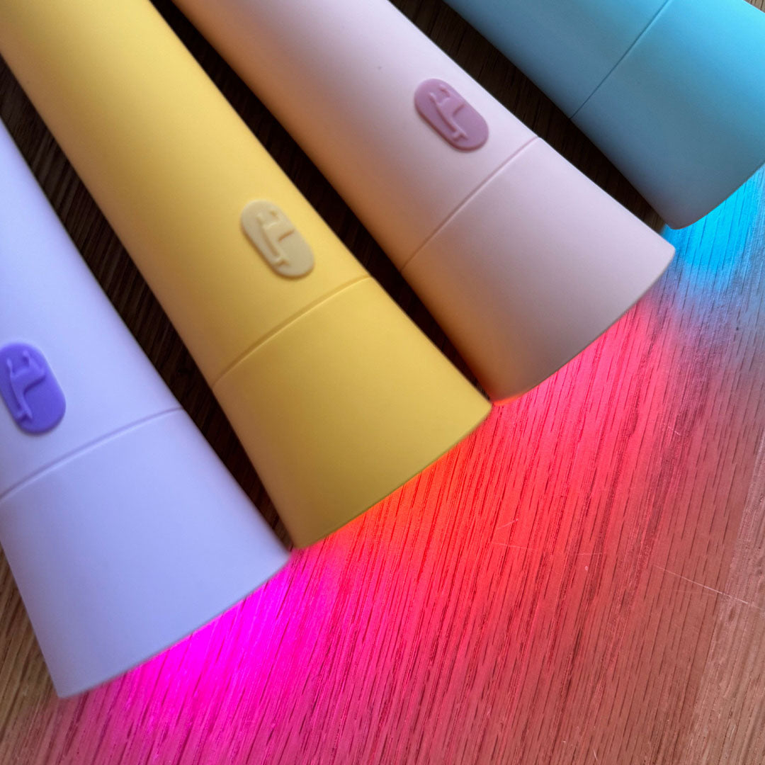 Close-up van de voorkanten van vier Lalarma zaklampen in pastelkleuren die gekleurd licht schijnen op een houten ondergrond.