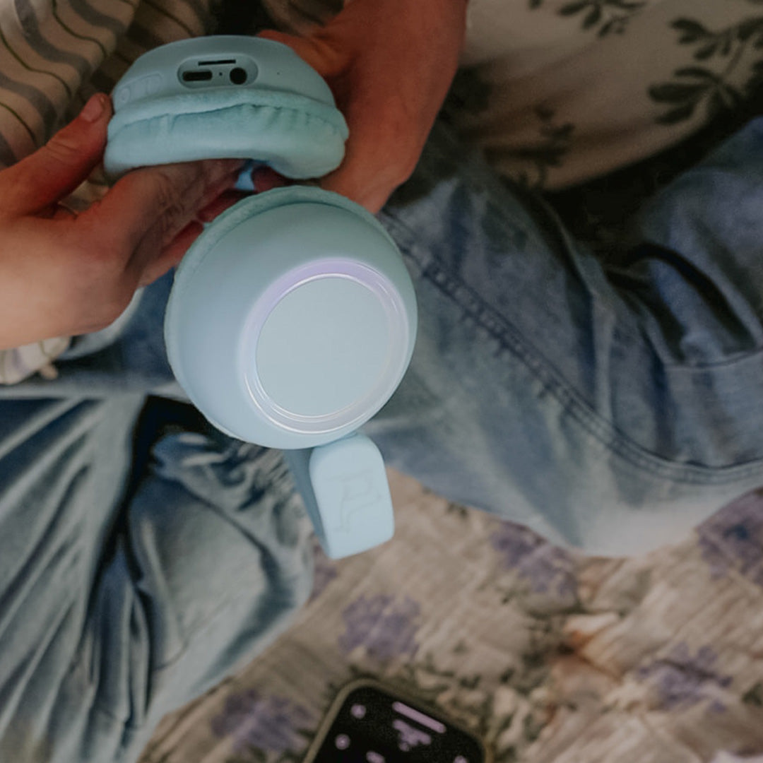 Handen houden een lichtblauwe Lalarma Copenhagen kinderkoptelefoon vast met een oplichtende ring op de oorschelp.