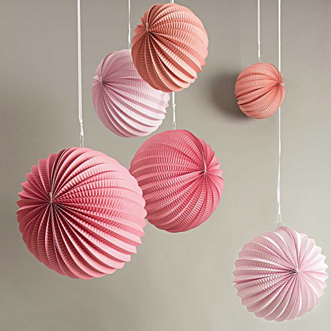 Meerdere roze en perzikkleurige papieren lampions hangen aan witte linten.