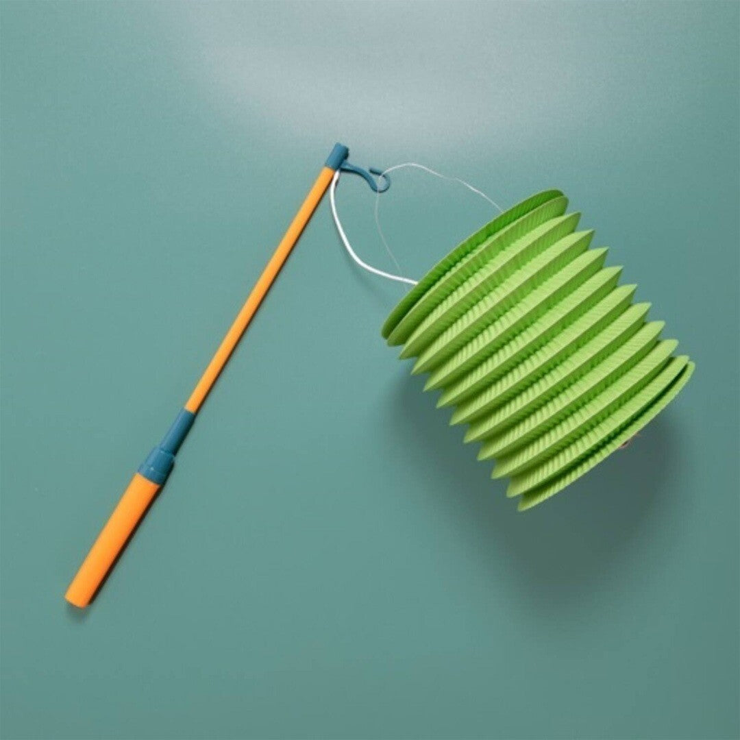 Folat lampionstokje in oranje en groen houdt een groene opvouwbare lampion vast op een teal achtergrond.