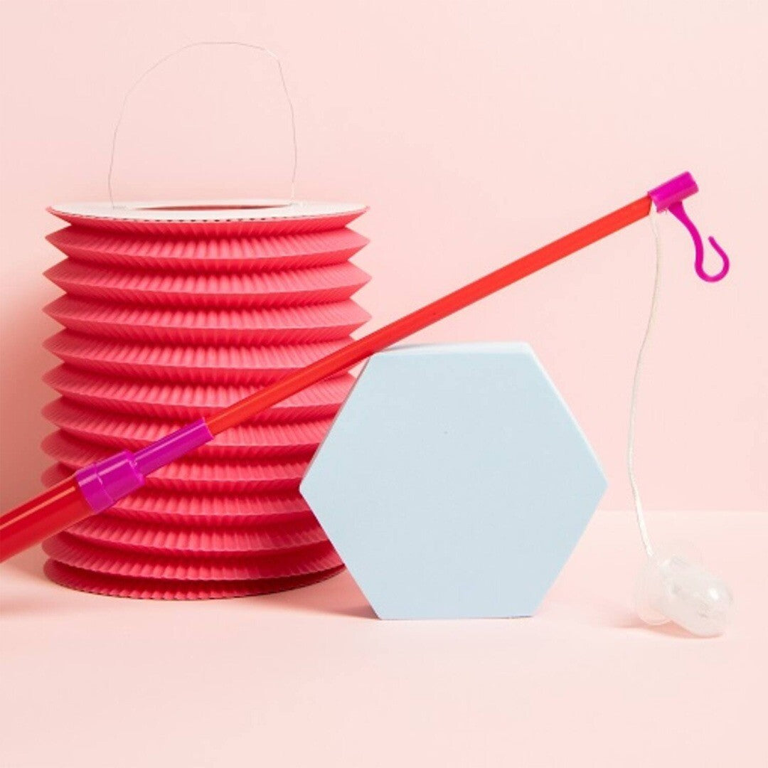 Folat rood lampionstokje leunt tegen een blauw zeshoekig blok, naast een roze opvouwbare lampion.