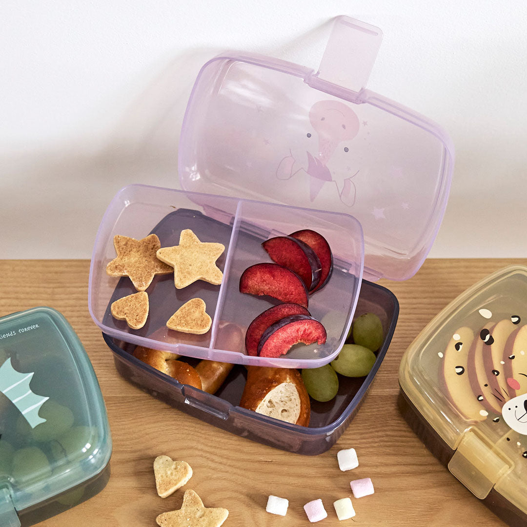 Een open Lässig kinderbroodtrommel gevuld met koekjes, fruit en brood, met een uitneembaar compartiment.