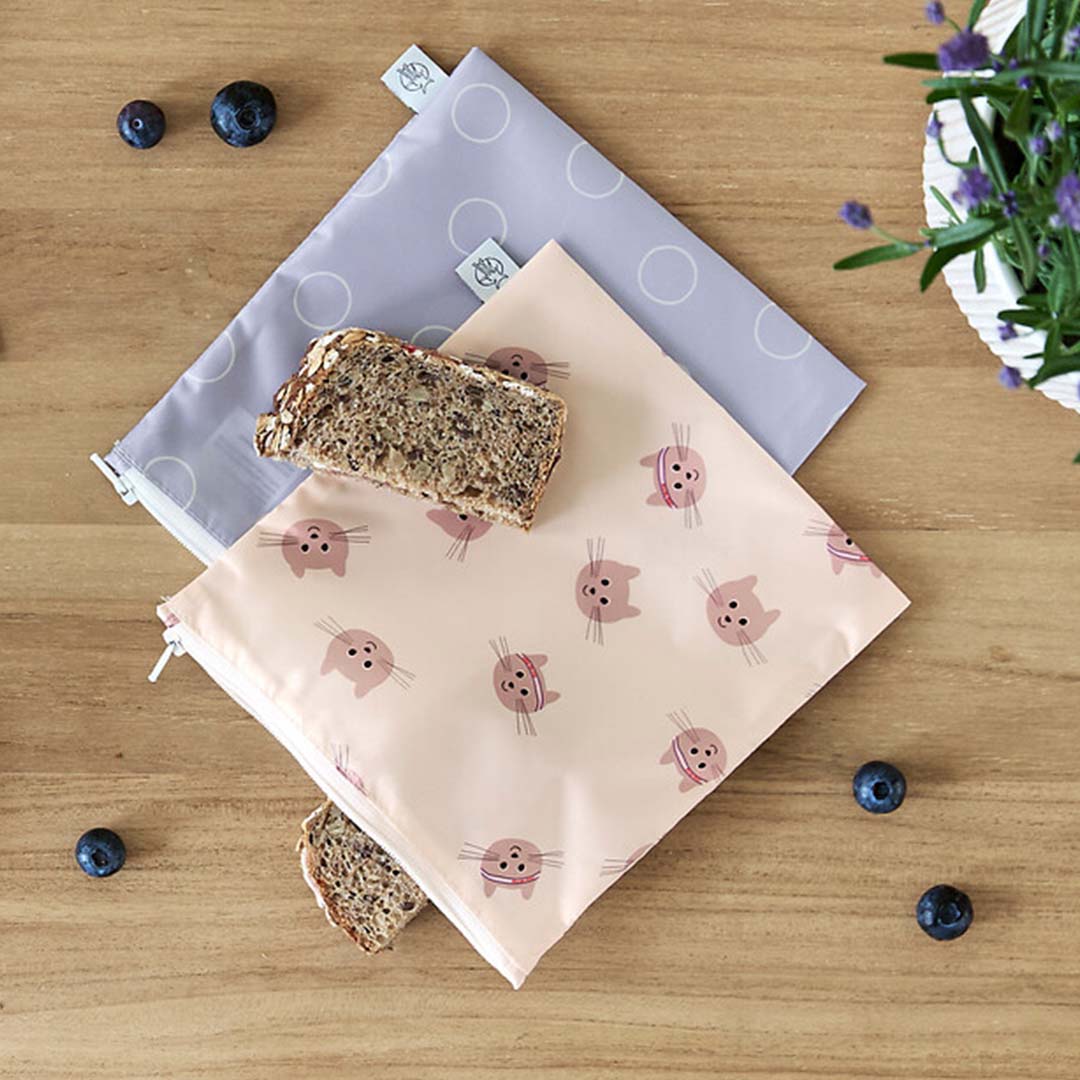 Lässig herbruikbare snackzakjes op een houten tafel, één met brood en bosbessen.