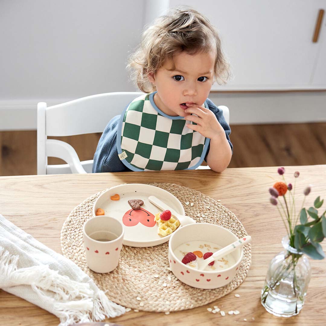 Een peuter zit aan tafel met een lässig kinderbord, kom en beker tijdens het ontbijt.