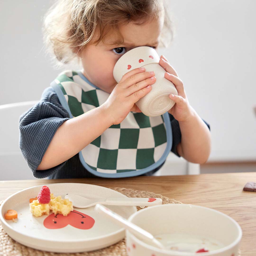 Een peuter drinkt uit een lässig kinderbeker met hartjespatroon aan de ontbijttafel.