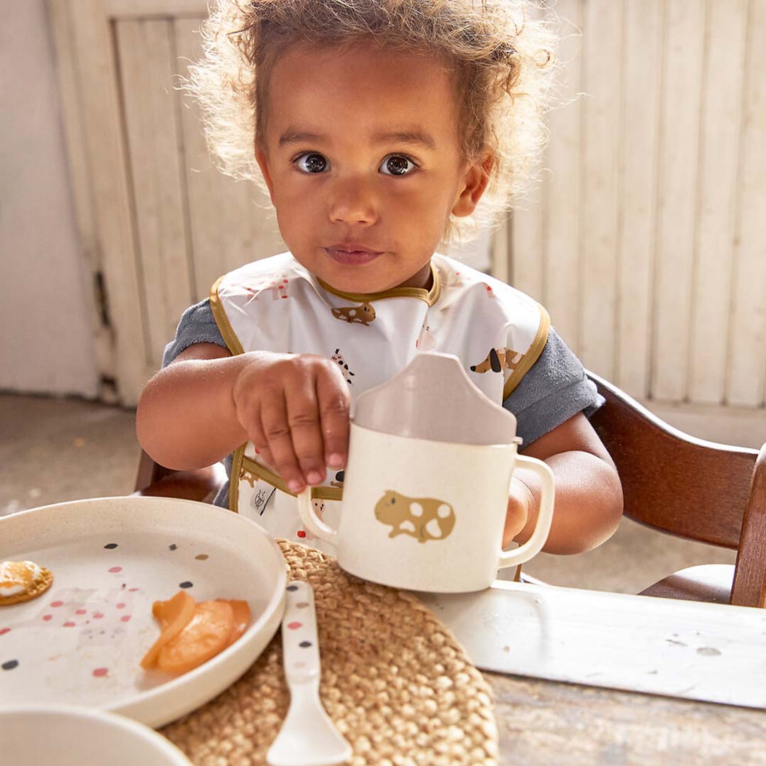 Een peuter zit aan tafel met een Lässig kinderbord en een beker.