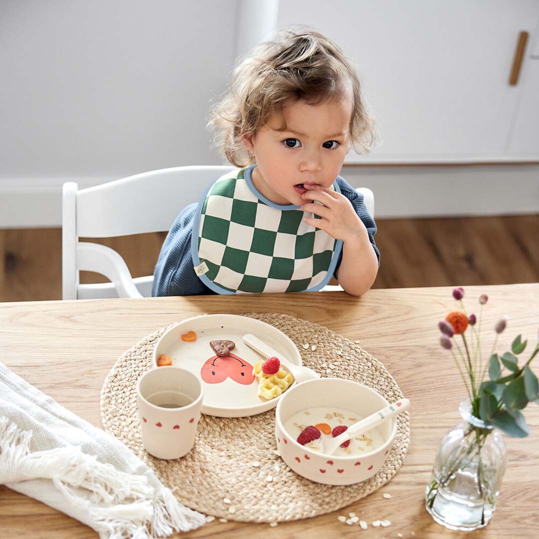 Peuter zit aan tafel met lässig kinderservies met hartjes en een gezichtje.