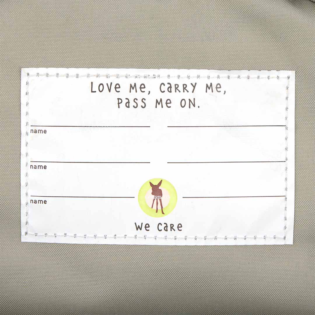 Detail van de Lässig kleuterrugzak met een label waarop 'Love Me, Carry Me, Pass Me On' staat.