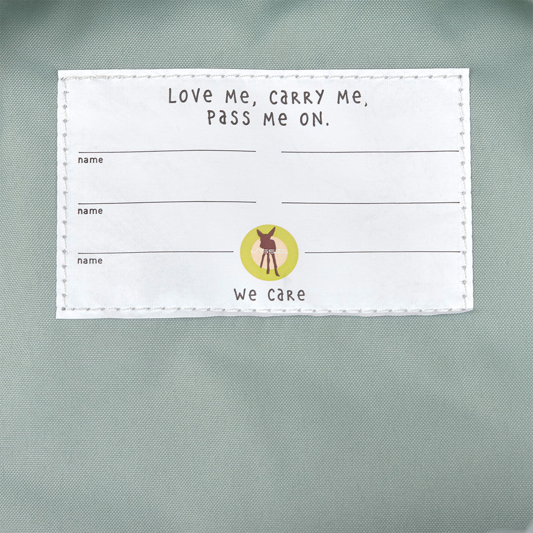 Detail van een wit label in de rugzak met de tekst 'Love me, carry me, pass me on'.