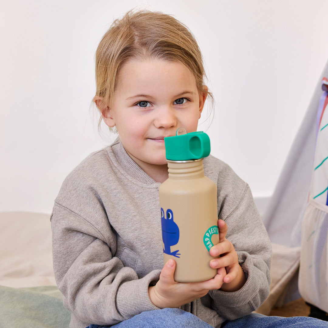 Een lachend meisje houdt de Lässig kinderdrinkfles met kikkerillustratie vast.